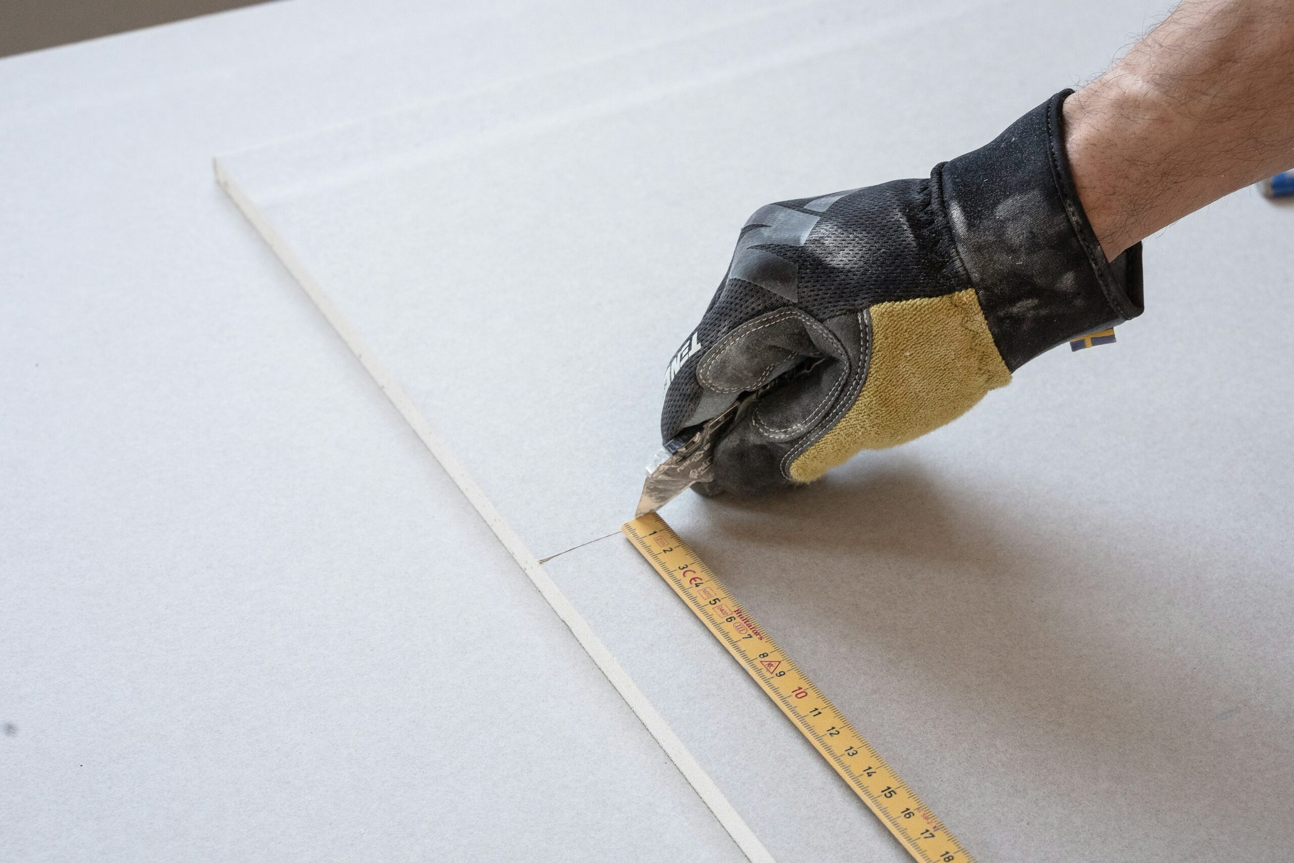 A carpenter cuts a board with Ten Protection work gloves on.