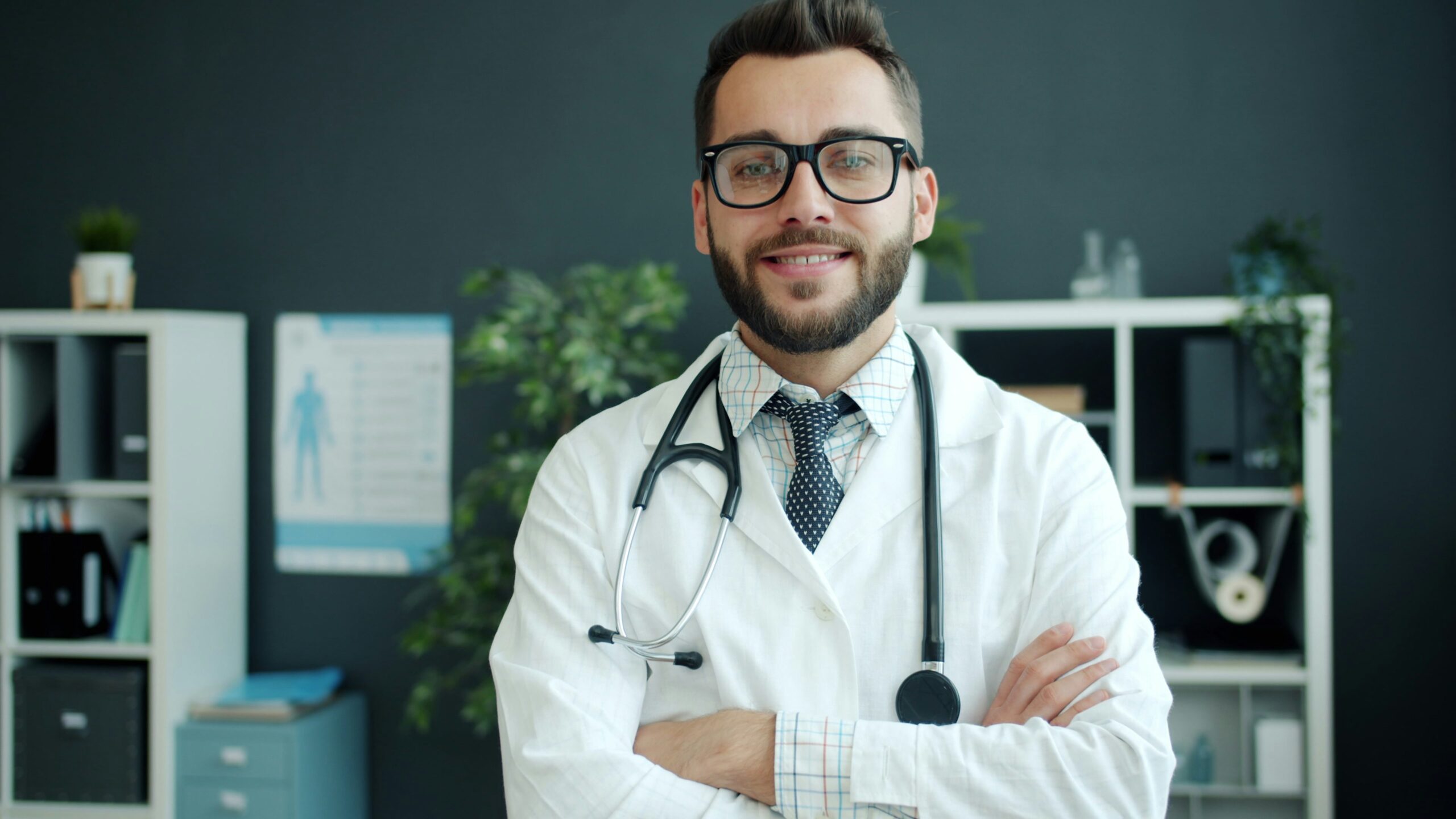 Portrait of friendly young guy doctor smiling standing in office with arms crossed looking at camera. Professionals, emotions and people concept.