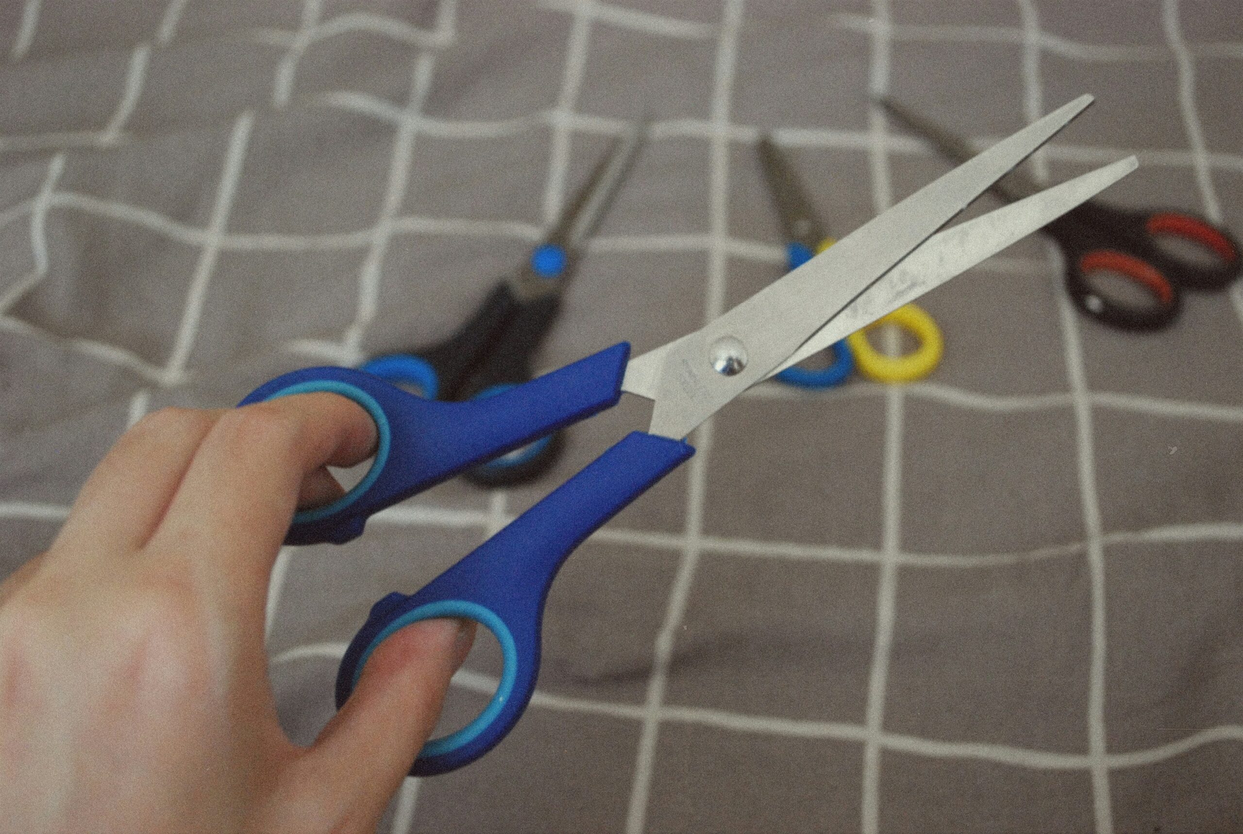 The hand that holds blue scissors, other scissors on the background